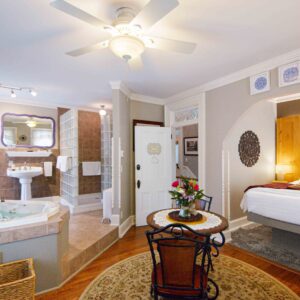 Spacious view of the Colonel Park Suite, a romantic getaway at the Main Street Inn, featuring the queen bed, sitting area, dining table, and jacuzzi tub in an elegant open layout.