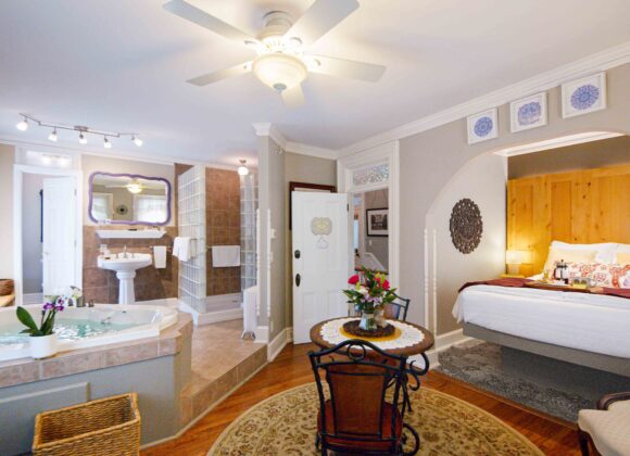 Spacious view of the Colonel Park Suite, a romantic getaway at the Main Street Inn, featuring the queen bed, sitting area, dining table, and jacuzzi tub in an elegant open layout.