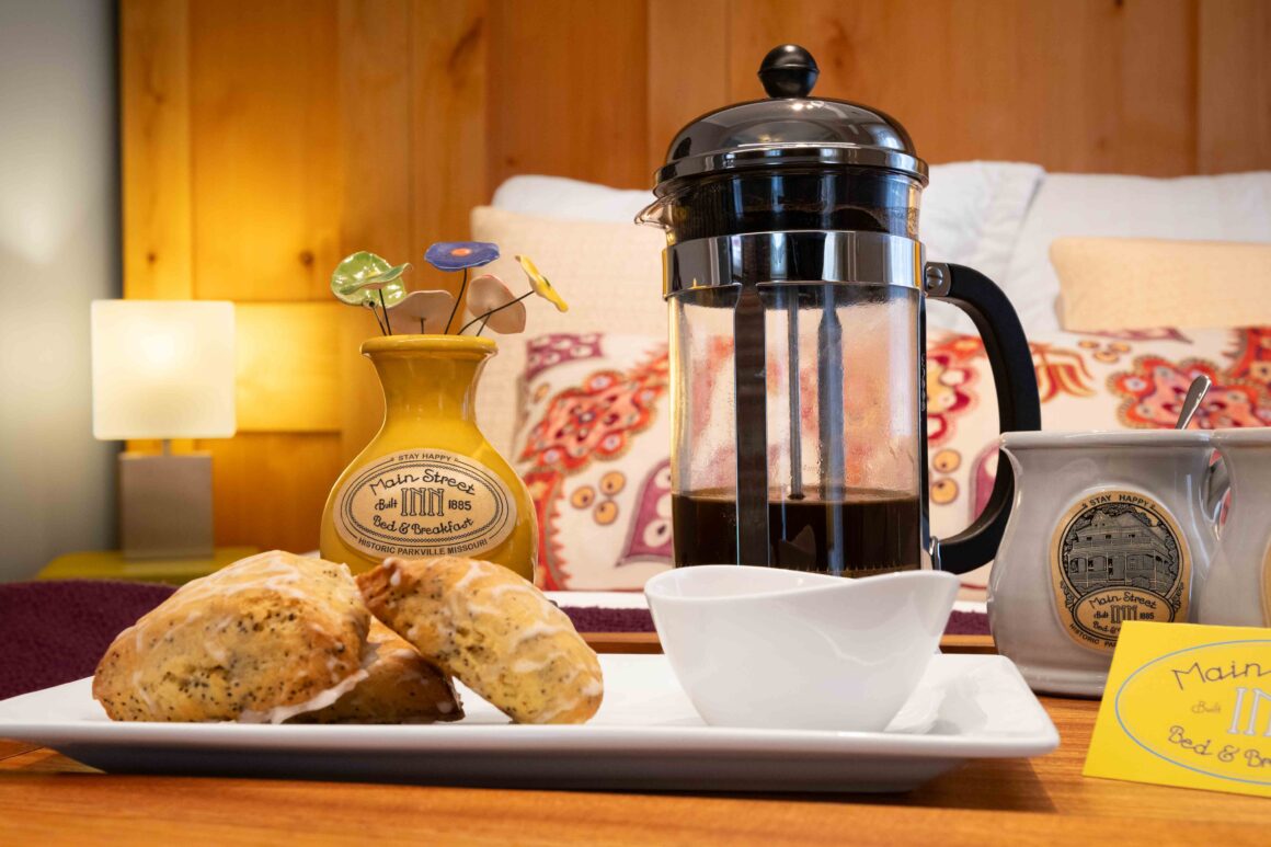 Close-up of a breakfast tray with a French press, pastries, and Main Street Inn pottery on the bed in the Colonel Park Suite.