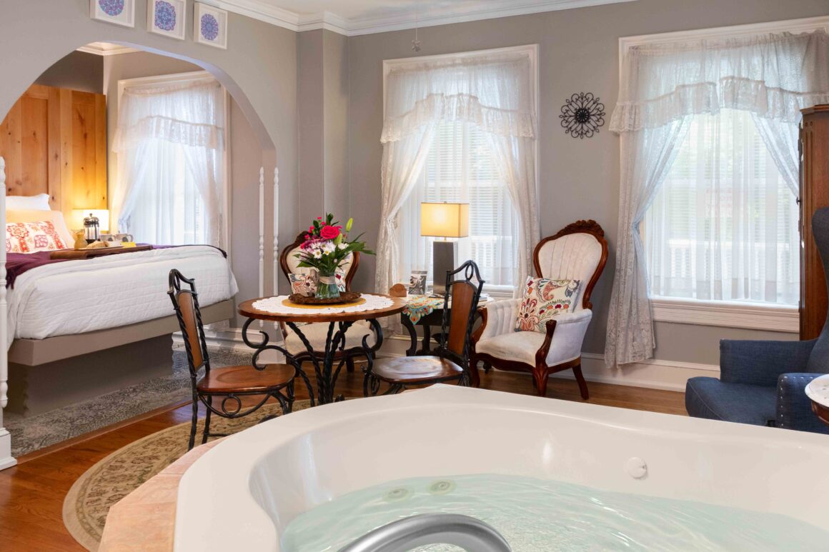 View of the jacuzzi tub in the foreground with the bed and sitting area of the Colonel Park Suite in the background.