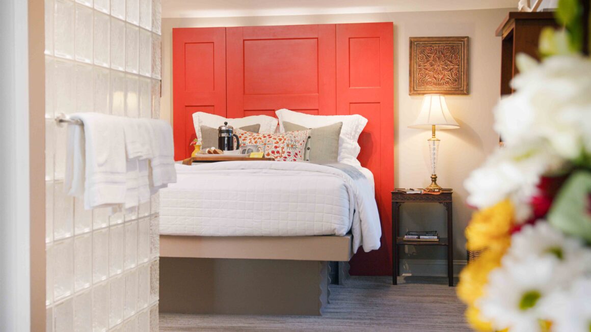 A welcoming view of the Missouri River Suite featuring the bed with red headboard, glass block wall, and soft florals in the foreground.