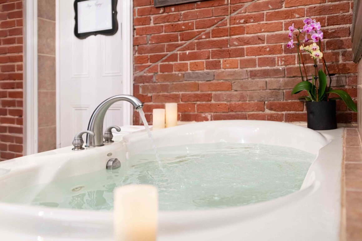 Water flowing into the jetted tub beside the exposed brick wall.