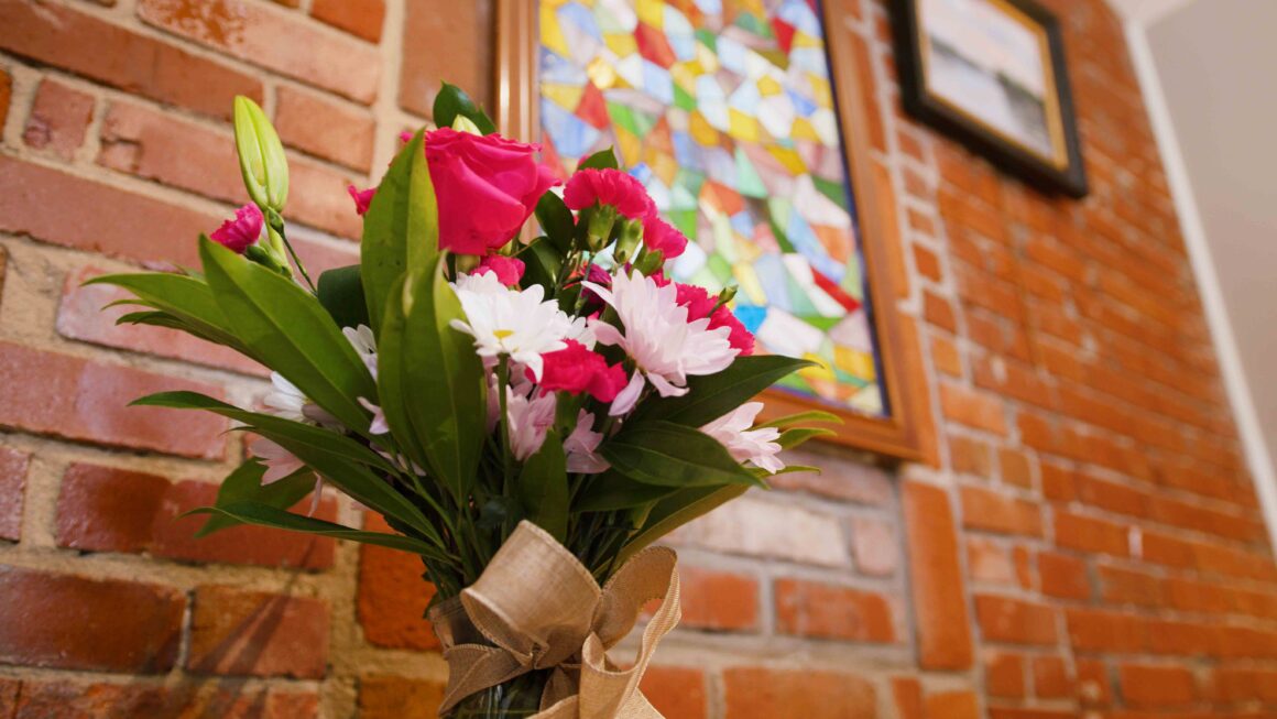 Bouquet of pink and white florals in front of brick wall and colorful stainglass.