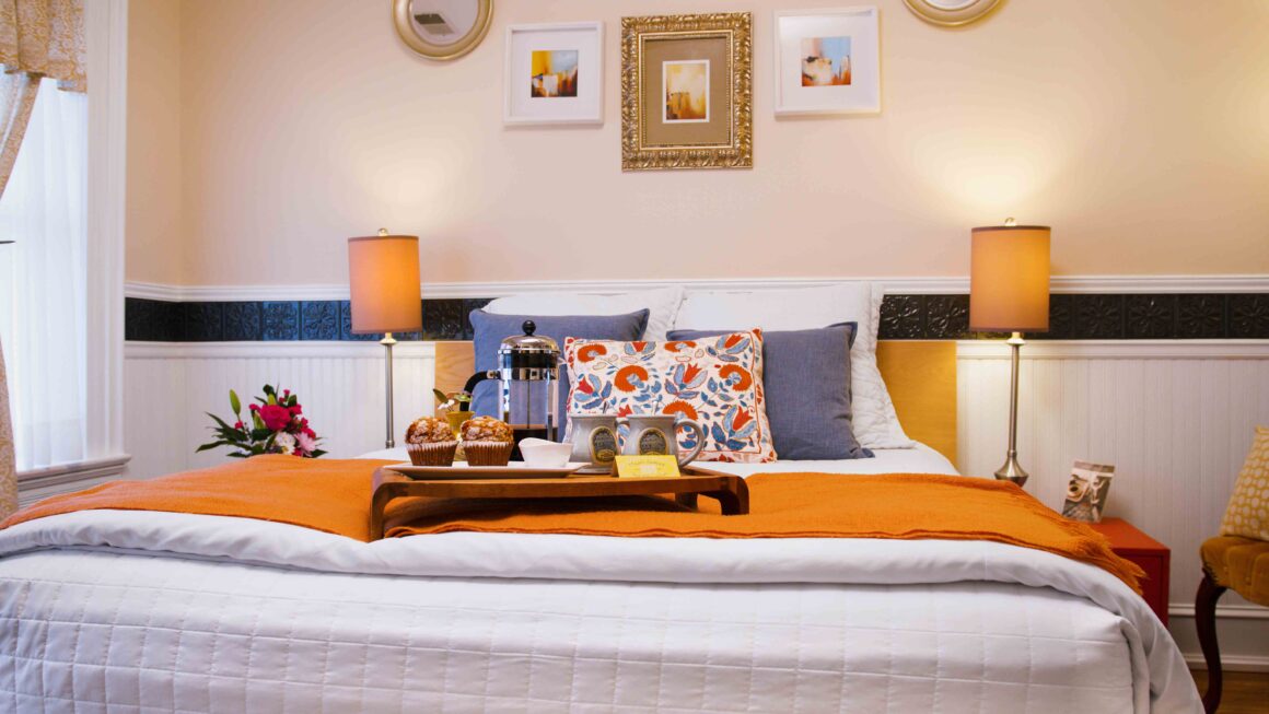 Cozy bed in Old Kate’s Room with colorful pillows, warm lighting, and curated wall décor.